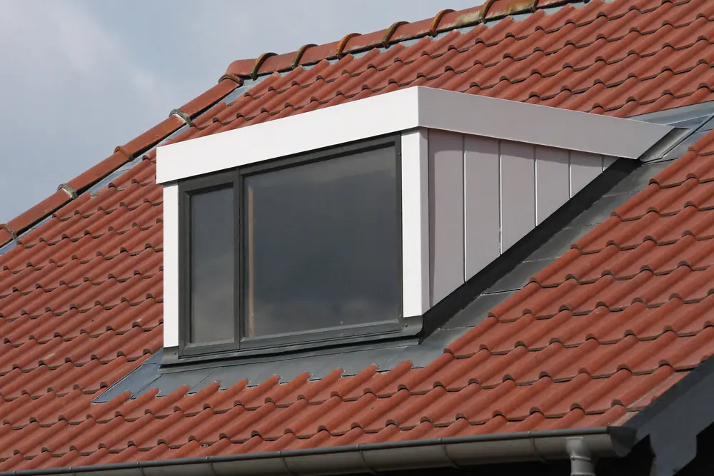 Witte kunststof dakkapel met antracietkleurige kozijnen op een rood pannendak